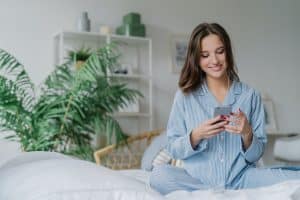 Happy woman with appealing look, holds modern cell phone, downloads song to playlist